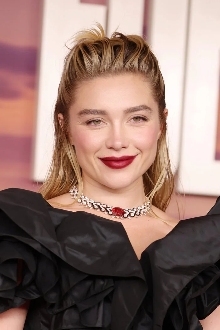 Person wearing an elegant black ruffled dress and a jeweled necklace, smiling at a formal event
