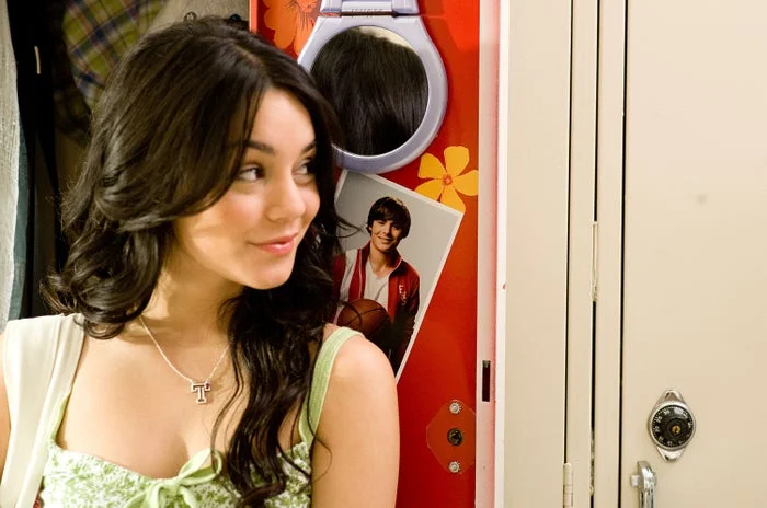 Person in a casual setting looking to the side, wearing a necklace. Locker with a poster of a person holding a basketball in the background