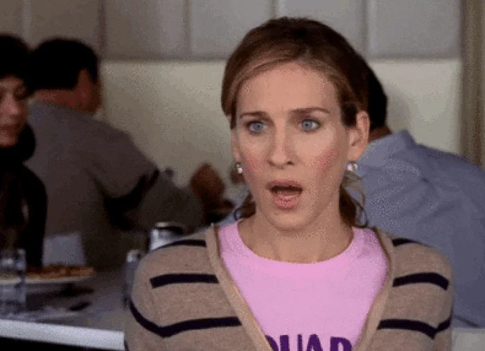 Person with wide eyes and open mouth, wearing a casual outfit with a striped cardigan, looking surprised or shocked indoors